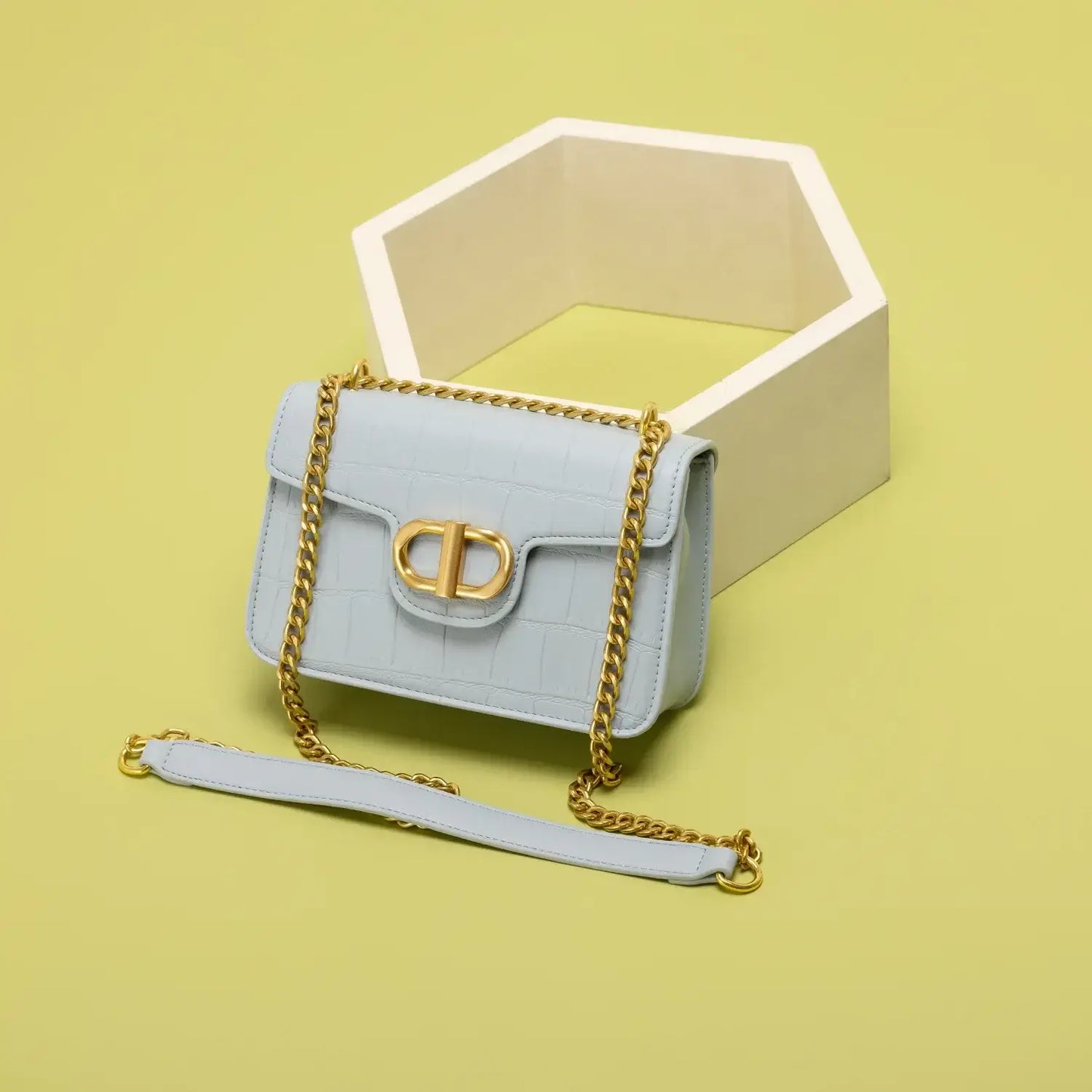 Light blue handbag with gold chain strap on a yellow background, featuring a stylish clasp and embossed pattern.
