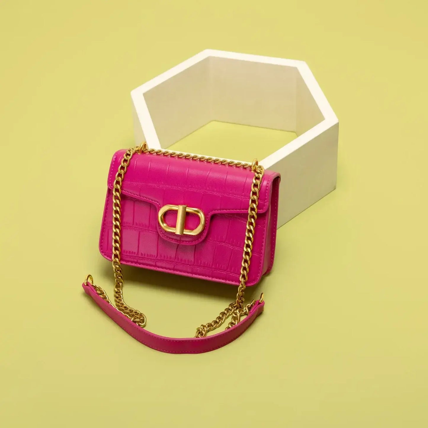 Pink crocodile texture handbag with gold chain strap against a yellow background.