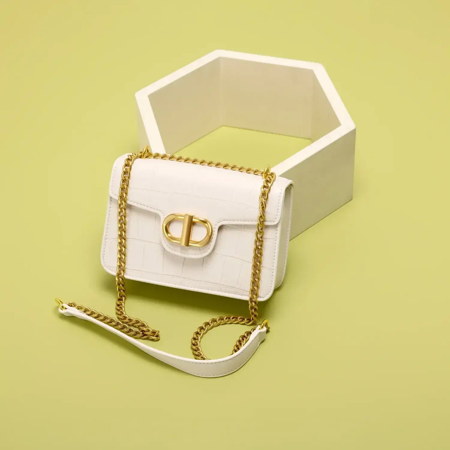 Stylish white crossbody bag with gold chain, placed on a geometric background, perfect for women.