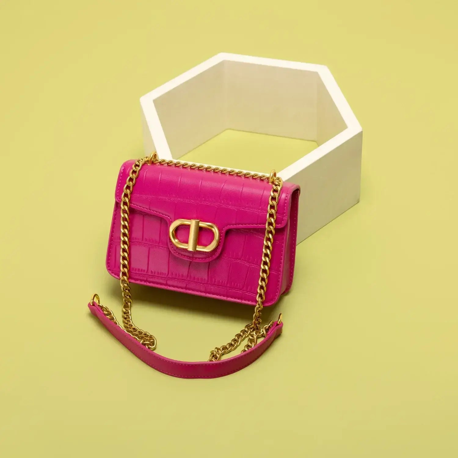 Pink crocodile texture handbag with gold chain strap against a yellow background.