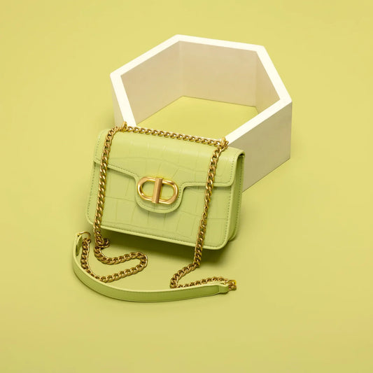 Light green handbag with gold chain strap, placed next to a white hexagonal decoration on a soft yellow background.